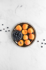 A top down view of apricots and a small bowl of blueberries on a metal tray. A complimentary colour concept.