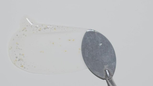 transparent serum gel with golden particles smudged by spatula Top view cosmetic texture