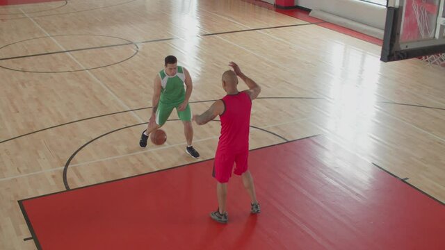 Handsome african american basketball player in uniform passing by opposing defender with dribbles, jumping, laying up and scoring field goal after bank shot during indoor basketball game.