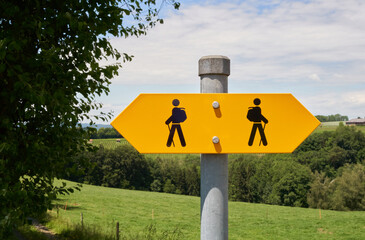 Bright yellow hiking trail signs arrows with two hiker figures pointing in opposite directions on an iron sign post in Switzerland.