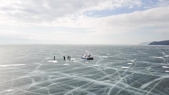 Group of people standing on cracked stnning ice lake near hovercraft. Clip. People travel and explore the frozen Baikal Lake in a safe and comfortable hovercraft.