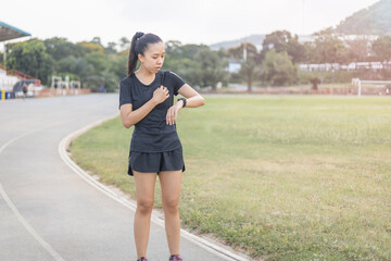 Women are tired after running hard on the running track. She is touching on the heart area and watching to smartwatch.