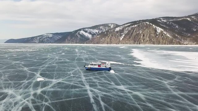 Group of people standing on cracked stnning ice lake near hovercraft. Clip. People travel and explore the frozen Baikal Lake in a safe and comfortable hovercraft.
