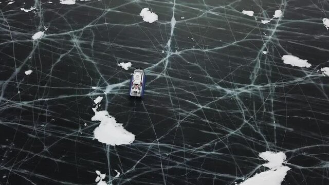 Typical hovercraft vehicle travelling across icy lake in winter. Clip. Top aerial view of the air cushion vehicle going into a skid on clear craked ice surface, lake Baikal, Siberia, Russia.