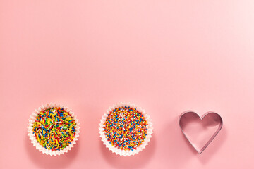Cupcake liners with colored sugar inside and heart shaped cutter on bottom from above. Flat lay top...