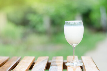 A glass of fresh cow's milk is placed on a wooden table next to the skies on a natural green ground.
