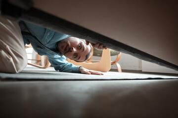 Under his bed in bedroom. Caucasian young man looking for job in unusual places at his home. Crazy,...