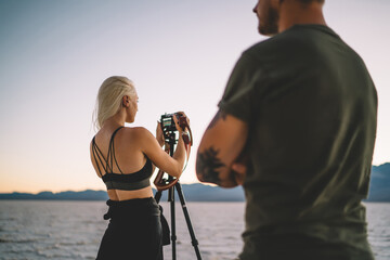 Back view of female photographer checking settings on camera for taking photo of night landscape in Badwater basin,skilled hipster girl and guy  having expedition in Badwater basin shooting video.