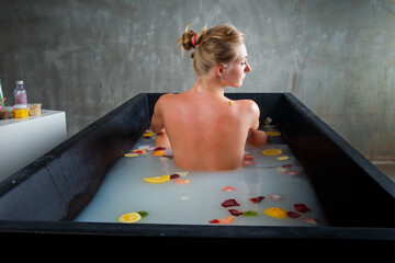 young beautiful blond woman taking bath with milk, rose petals and citrus slices