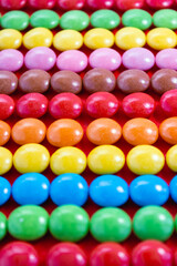 Milk colored chocolate folded in colored rows. Close-up of sweets on a red background. Vertical wallpaper. Selective focus
