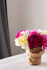 Beautiful bouquet of peonies stands on a white table against a background of gray curtains and a white wall