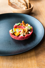 Fresh traditional polish beef tartar served with mushrooms, mustard and fresh lettuce on black ceramic plate ready to be served