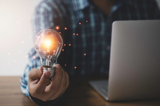 Businessman hand holding lightbulb with orange glowing and creative idea to laptop.
