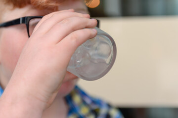 Cute red-haired boy with glasses in an urban context drinks ice water with lemon and ice. The boy with glasses drinks ice water.
