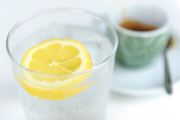 Glass of sparkling water with lemon and cup of coffee. Iced mineral water with lemon and cup of coffee on the white table.