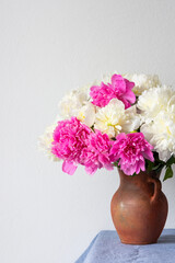 Beautiful bouquet of peonies in a clay pot stands on a table with a blue linen tablecloth