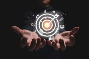 Hand holding virtual infographic target board with business icons such as graph coin Yuan and dollar. Objective target and investment goal concept.