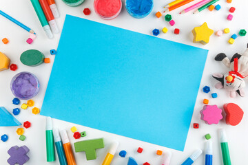 Top view of white tabletop with various drawing tools, finger paints, toy cow, blue paper sheet. Mock up. Children's drawing table.