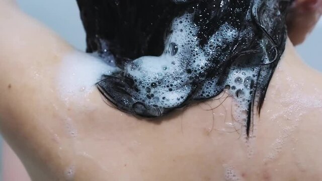 young brunette girl washes the shampoo out of hair with water shower in the bathroom