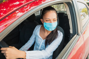 Shot of young woman wearing face mask while driving her car during coronavirus pandemic.