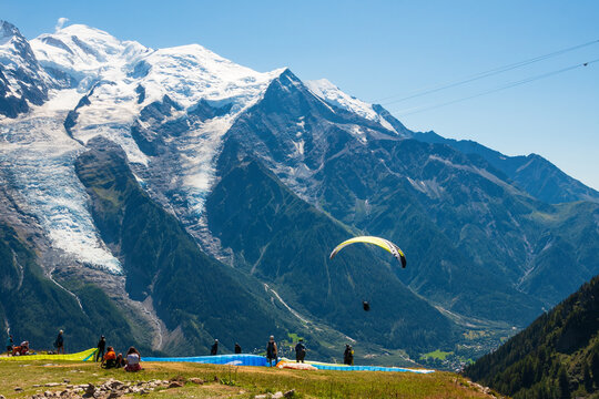 Planpraz, Chamonix, Savoie, France.  Paragliders fly, people hiking  with view of snow covered Mont Blanc mountain. Summer vacation recreation in French Alps. Active tourism background.