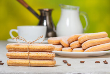 Italian savoiardi cookies or ladybugs cookies on a plate and tied with a rope, a white cup cup of coffee and a jug of milk in the background. Selective focus.