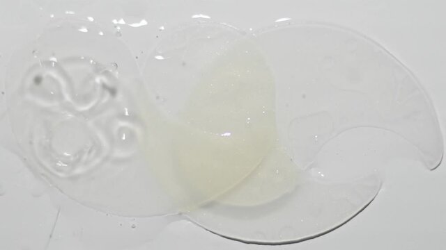 white transparent under eye patches and a liquid serum pouring on it from above. Top view slow motion from 120 fps