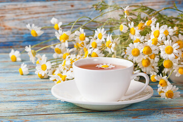 Daisy flowers in a white cup of tea, chamomile herbs on wooden background. Herbal medicine. Healthy lifestyle concept.