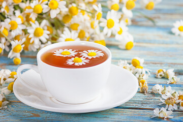 Herbal tea of chamomile flower and a bouquet of Matricaria chamomilla on on a blue wooden...