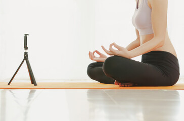 Young woman exercising at home doing yoga and looking at her smartphone.