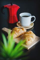 Breakfast there is a coffee maker, coffee white cup and croissants.