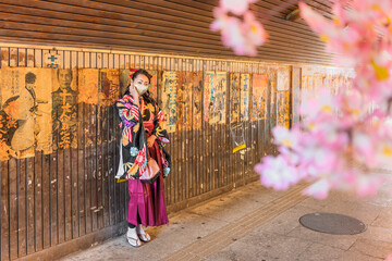 Fototapeta premium Japanese woman in hakama kimono wearing a cloth mask at retro underpass Yuraku Concourse decorated with old posters and placards glued to the walls of the tunnel who revive the nostalgic Showa era.