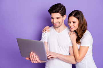 Photo pretty lady handsome guy married couple good mood hold notebook hands watch movie film together speak skype relatives wear casual white t-shirts isolated purple color background