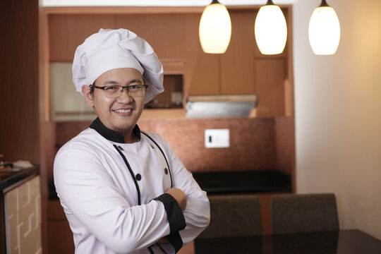 Portrait of happy proud Asian chef smiling at camera with crossed arms, chef in kitchen