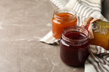 Napkin and glass jars with jam on gray background, space for text