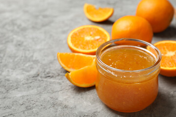 Oranges and glass jar with jam on gray background, close up