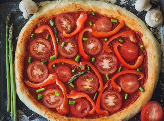 On the baking tray is a vegetarian pizza with tomatoes, peppers, mushrooms and asparagus. Home cooking. Pizza preparation.