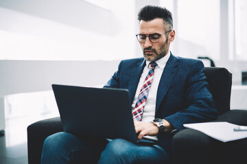 Concentrated mature entrepreneur in formal wear working at modern lapto computer and checking mail via 4G internet.Confident proud ceo 50 years old searching information on website on modern netbook