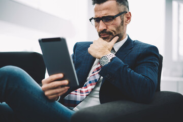 Concentrated middle aged trader in formal wear reading attentively financial news on website on...