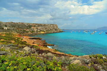 Fototapeta premium paradise clear torquoise blue water with boats and cloudy blue sky in background in Favignana island, Cala Rossa Beach, Sicily South Italy.