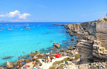 paradise clear torquoise blue water with boats and cloudy blue sky in background in Favignana island, Cala Rossa Beach, Sicily South Italy.