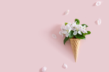 Spring background. Ice cream cone with white flowers and leaves on pink background. Summer concept. Flat lay, copy space. Sale, greeting card, poster, banner concept.