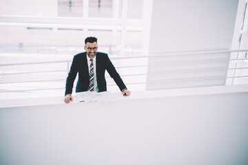 Top view of positive successful proud ceo 50 years old smiling at camera while working with text documents indoors in company.Prosperous mature entrepreneur in formal wear standing with reports