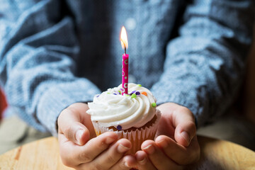 close up of hands and birthday cupcake with a candle