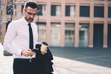 Successful mature business man dressed in formal clothes searching information about modern technology in social network on smartphone using 4G internet walking with coffee, mock up for your advertise