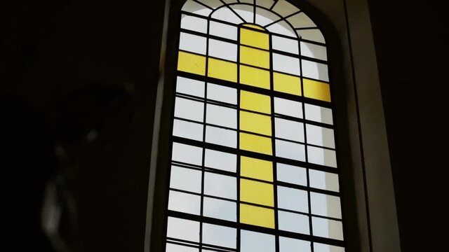 Stained-glass window, a yellow cross on the church window is created from white, transparent and colored glass