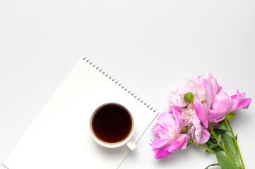 Obraz na płótnie Canvas Cup of black morning coffee, blank clean white notepad album, beautiful pink peonies flowers on gray background. Top view flat lay copy space. Female desktop, breakfast, time for planning