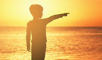 contour of a boy at sunrise sunset on the seashore of the ocean orange sky sea ocean boy shows his finger to the side