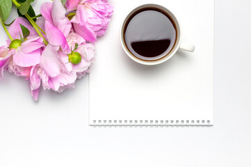 Cup of black morning coffee, blank clean white notepad album, beautiful pink peonies flowers on gray background. Top view flat lay copy space. Female desktop, breakfast, time for planning