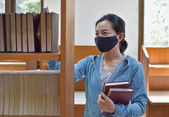 Woman in medical mask search a book in a library